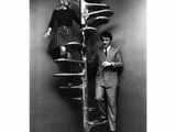 a black and white photo of a man and a woman standing next to a spiral staircase
