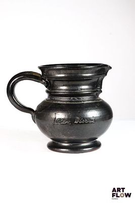 un vase noir muni d'une anse, posé sur une surface blanche