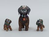 trois figurines miniatures représentant des chiens portant des colliers colorés, posées sur une surface blanche