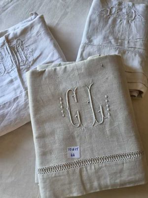 three white linen napkins with embroidered monograms on them