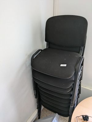a stack of black chairs next to a table with a laptop on it