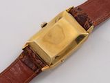a gold watch on a brown leather strap on a white surface