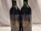 two bottles of red wine sitting on top of a white sheet