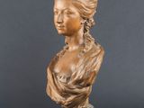 un buste en bronze représentant une femme aux cheveux longs, à côté de noix