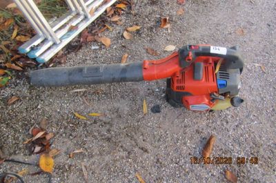 un souffleur de feuilles rouge posé par terre à côté d'une clôture