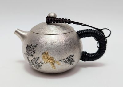 une théière en argent ornée d'un oiseau