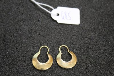 a pair of gold earrings on a black surface with a price tag