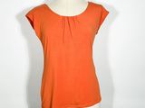 un haut orange posé sur un présentoir à mannequin, sur fond blanc