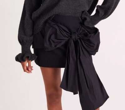 une femme portant un pull gris et une jupe noire, avec un nœud papillon