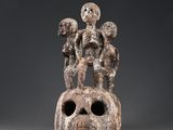 une sculpture représentant un crâne sur lequel sont perchées trois personnes