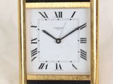une image représentant une horloge noire et dorée posée sur un drap blanc
