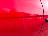 a close up of a red car door with a reflection of a person in the mirror