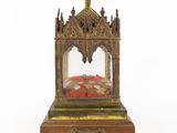 an antique brass clock with a red velvet cushion on a wooden stand