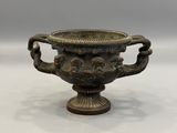 une image représentant un vase en bronze posé sur une surface blanche