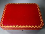 an old red box with gold trimming on it sitting on a table