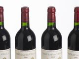 six bottles of red wine lined up in a row on a white surface