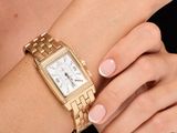 someone is wearing a gold wrist watch with a white dial