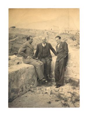 trois hommes assis sur un mur de pierre, dont l'un tient sa main