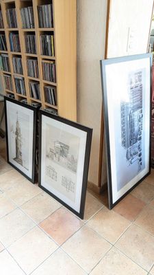 trois photos encadrées posées par terre à côté d'une bibliothèque
