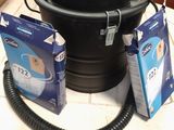 une photo d'un seau noir avec un tuyau d'arrosage et deux paquets de papier toilette
