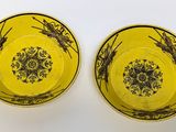 two yellow bowls with black designs on them on a white surface