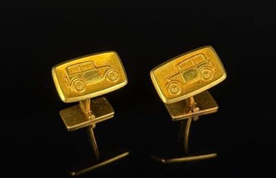 two gold cufflinks with a car on them on a black surface