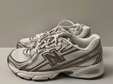 Les chaussures New Balance sont blanches et marron, avec des touches de marron.