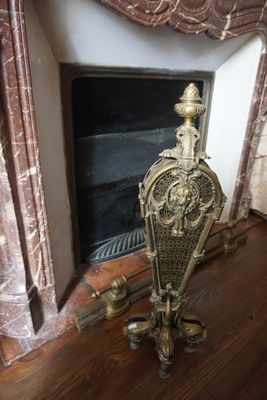une horloge en or posée sur un socle devant une cheminée