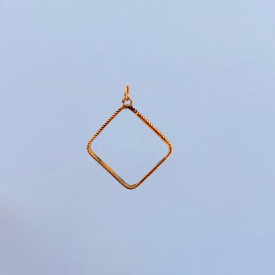 un pendentif carré en or suspendu à une chaîne, sur fond de ciel bleu