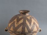 un vase marron orné d'un motif, à côté de quelques noix