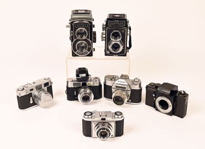 several old cameras are arranged in a row on a white surface