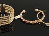 two gold bracelets and a bracelet with pearls on a black surface