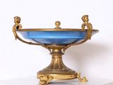 un bol en verre bleu posé sur un socle doré, lui-même posé sur une surface blanche
