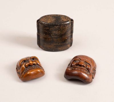 deux petits masques en bois et une boîte en bois posés sur une surface blanche
