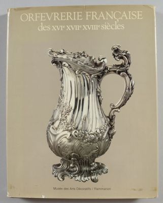 un vieux livre sur lequel est posé un vase en argent, posé sur une table