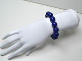 une main de mannequin blanche tenant un bracelet bleu en perles