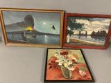 trois tableaux encadrés représentant des bateaux et des fleurs, exposés sur une table