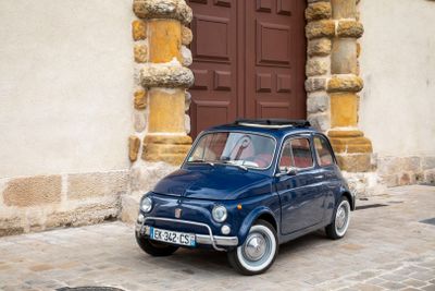 a small blue car parked in front of a brown door