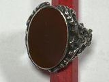 une bague en argent ornée d'une pierre marron posée sur un crayon rouge