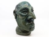 une sculpture verte représentant une tête d'homme sur une surface blanche