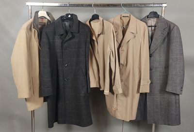 trois manteaux suspendus à un porte-manteau devant un mur gris