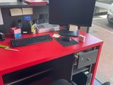 un bureau rouge avec une chaise noire et un ordinateur posé dessus