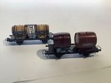 two toy train cars with barrels on them on a white surface