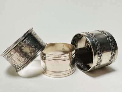 three silver napkins and a silver cup on a white surface