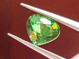 quelqu'un tient une pince dans laquelle est sertie un diamant vert