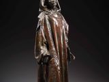 a bronze statue of a woman in a cloak and hat