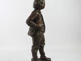 bronze statue of a boy in a hat and jacket standing on a wooden base