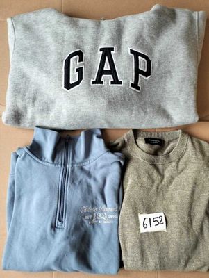 two pairs of sweaters with the word gap on them sitting on a cardboard box