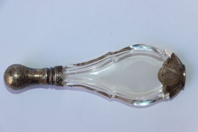 une cuillère en argent avec un manche en verre posée sur une surface blanche