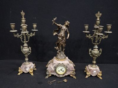 three antique bronze figurines and a clock on a black background